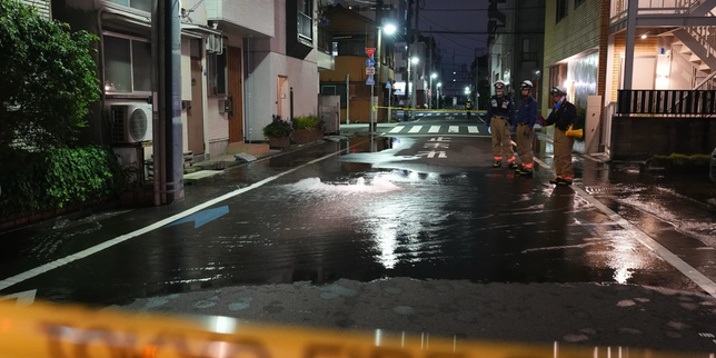 Tokyo firefighters stand on a partially flooded street after a water pipe ruptured following the earthquake in Tokyo on Aug. 23, 2026. - lemonde.fr