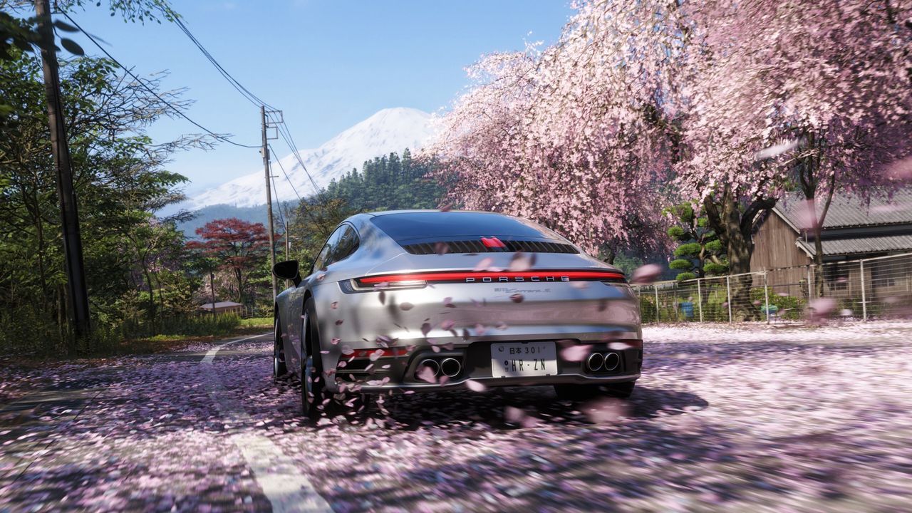 Cherry blossoms swirl around a silver car driving toward Mount Fuji in Forza Horizon 6. - gamesradar.com